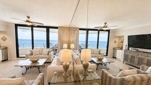 A spacious living room with a large TV, comfortable seating, and a view of the ocean. - West 1003 at Eden Condominiums Gulf Front Condo with Stunning Views! (Pensacola)