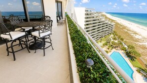 A balcony with a table and chairs, overlooking a beach and a hotel building. - West 1003 at Eden Condominiums Gulf Front Condo with Stunning Views! (Pensacola)