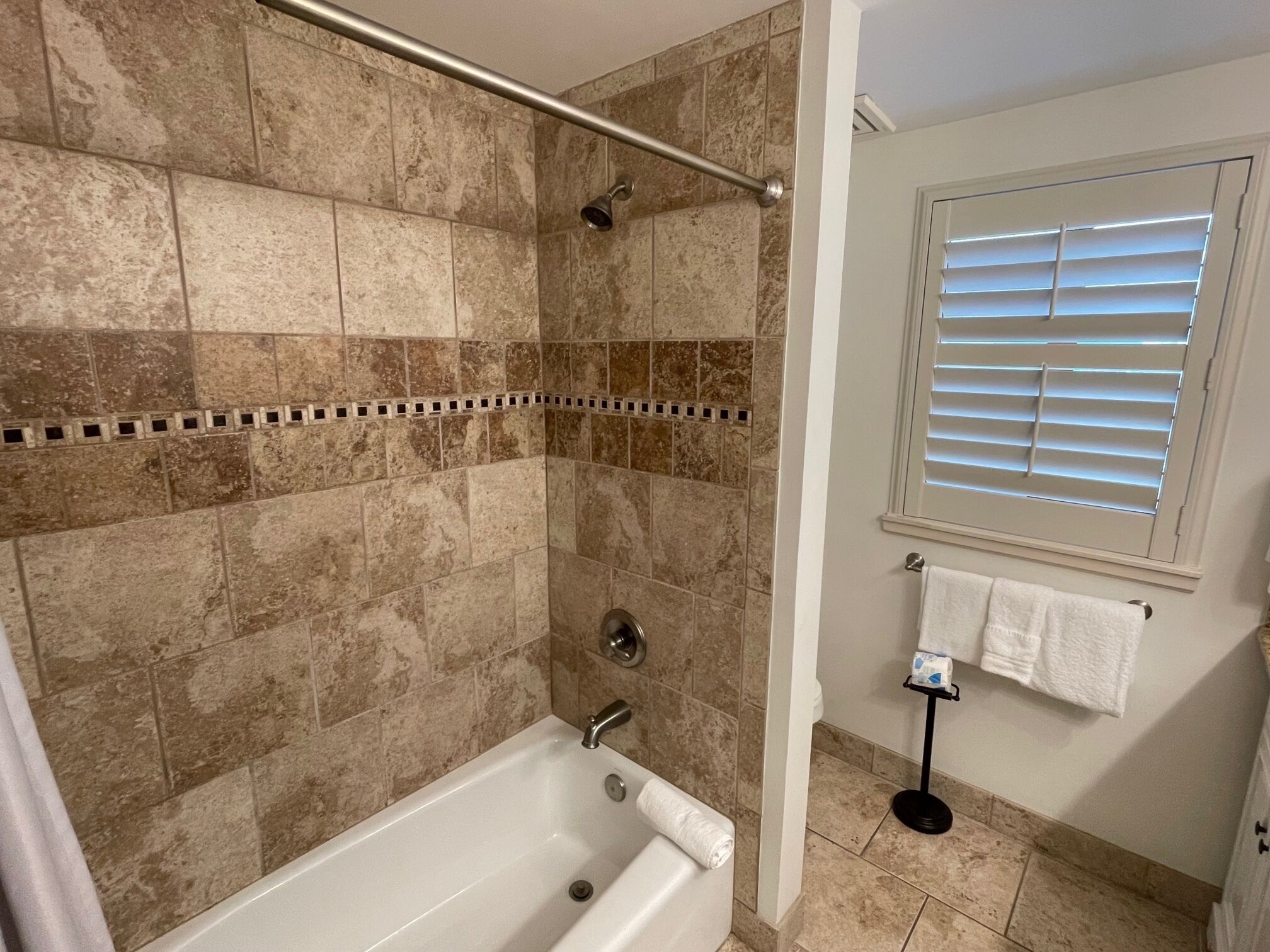 A bathroom with a bathtub, shower, and a window with blinds.