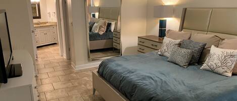 Een slaapkamer met een bed, nachtkastjes, een spiegel en een nachttafeltje.