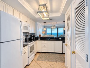 A kitchen with white cabinets, a black countertop, and a view of the ocean.