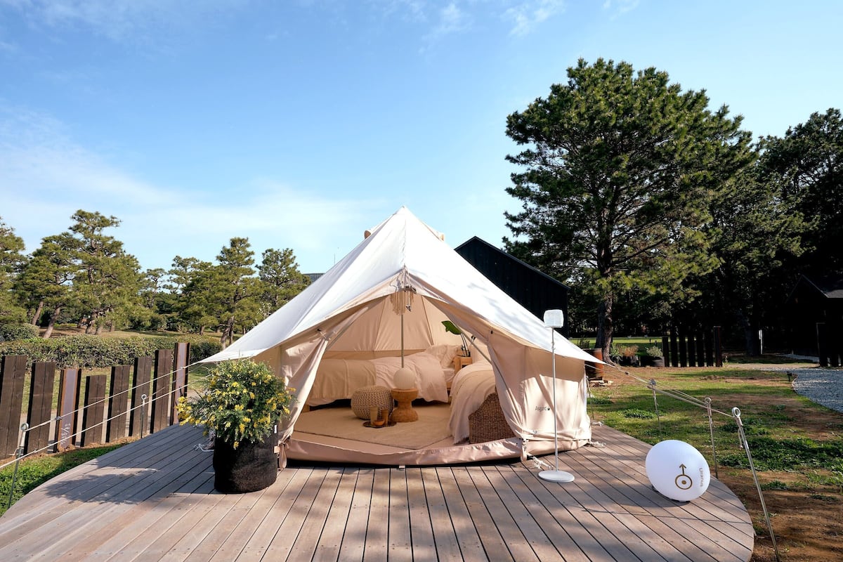 A tented accommodation with a wooden deck, a potted plant, and a directional sign.