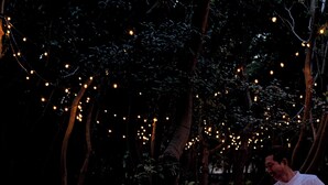 Un grupo de personas cenando en una mesa al aire libre con luces colgantes.