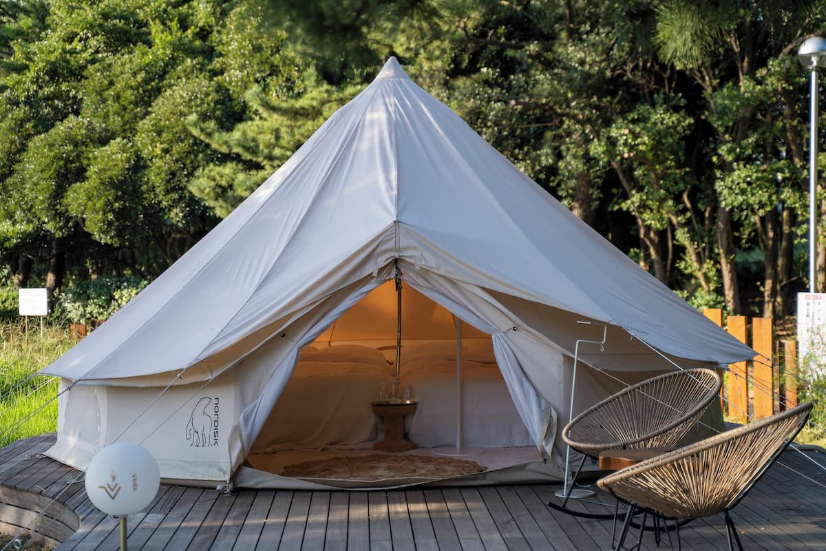 A tent with a central table and two chairs, surrounded by a wooden deck and greenery.