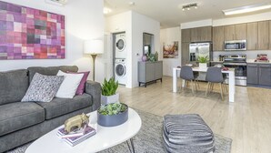 Eine moderne Wohnung mit grauem Sofa, einem runden Couchtisch, einem Essbereich und einer Küche mit grauen Schränken und Edelstahlgeräten.