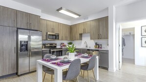 Eine moderne Küche mit Holzausbau, Edelstahlgeräten und einem Essbereich mit weißem Tisch und grauen Stühlen.
