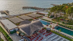 An aerial view of a resort with a large pool, beach umbrellas, and a pier extending into the water. - Siu Collection Ultra All Inclusive (Kemer)