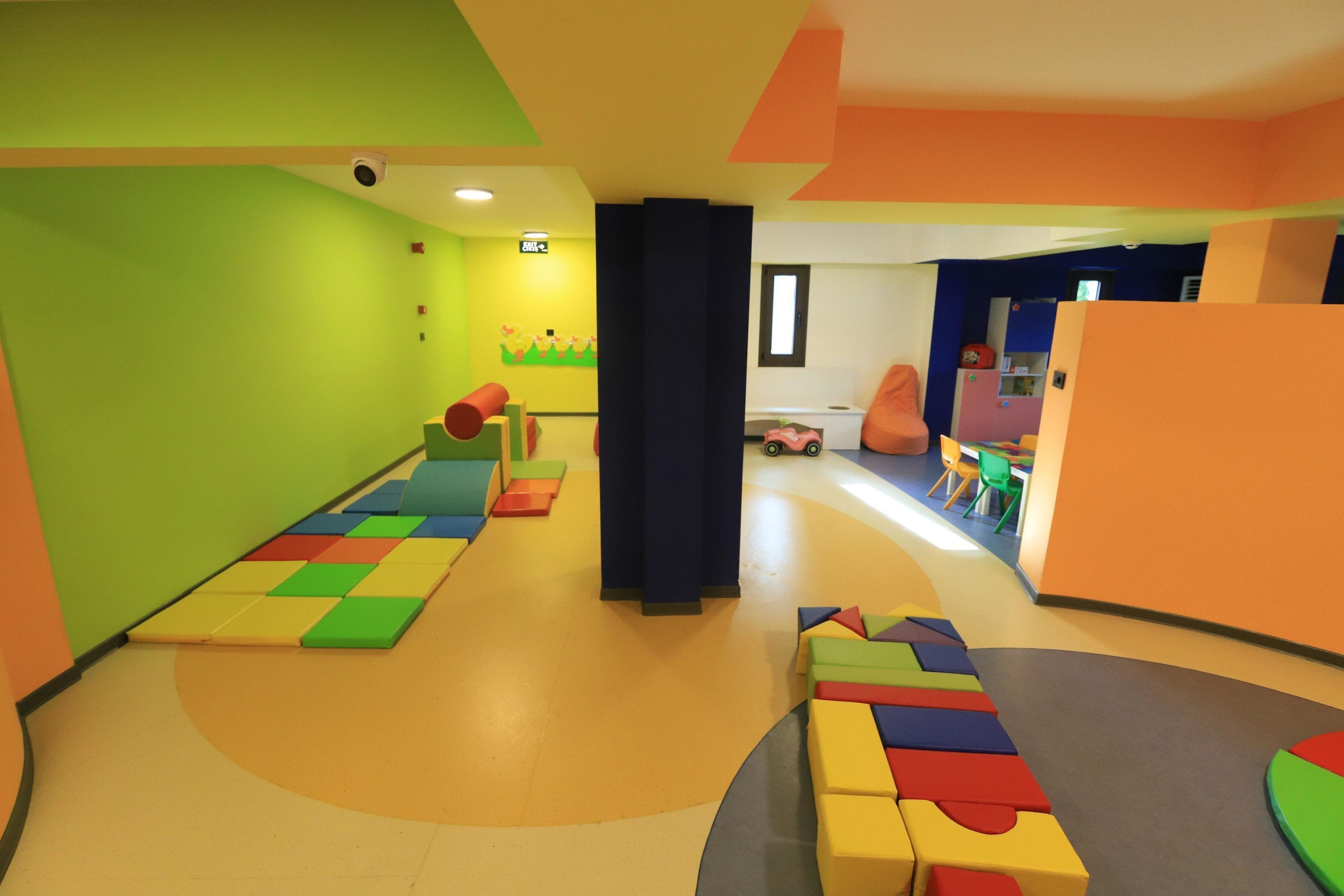Un'area giochi vivace e colorata con tappeti imbottiti, blocchi in schiuma e una piccola cucina giocattolo.