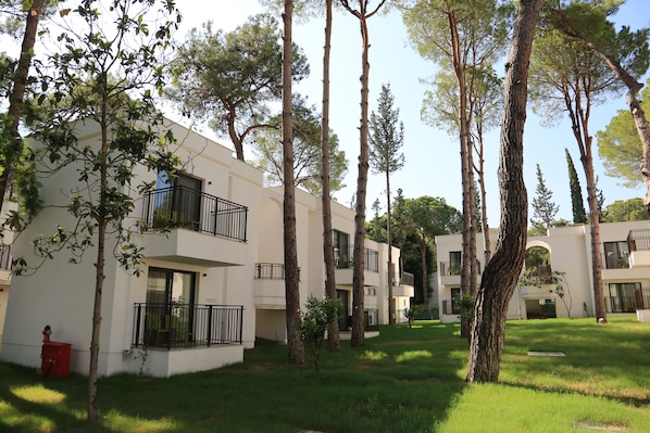 A residential building with multiple balconies, surrounded by tall trees and a well-maintained lawn.