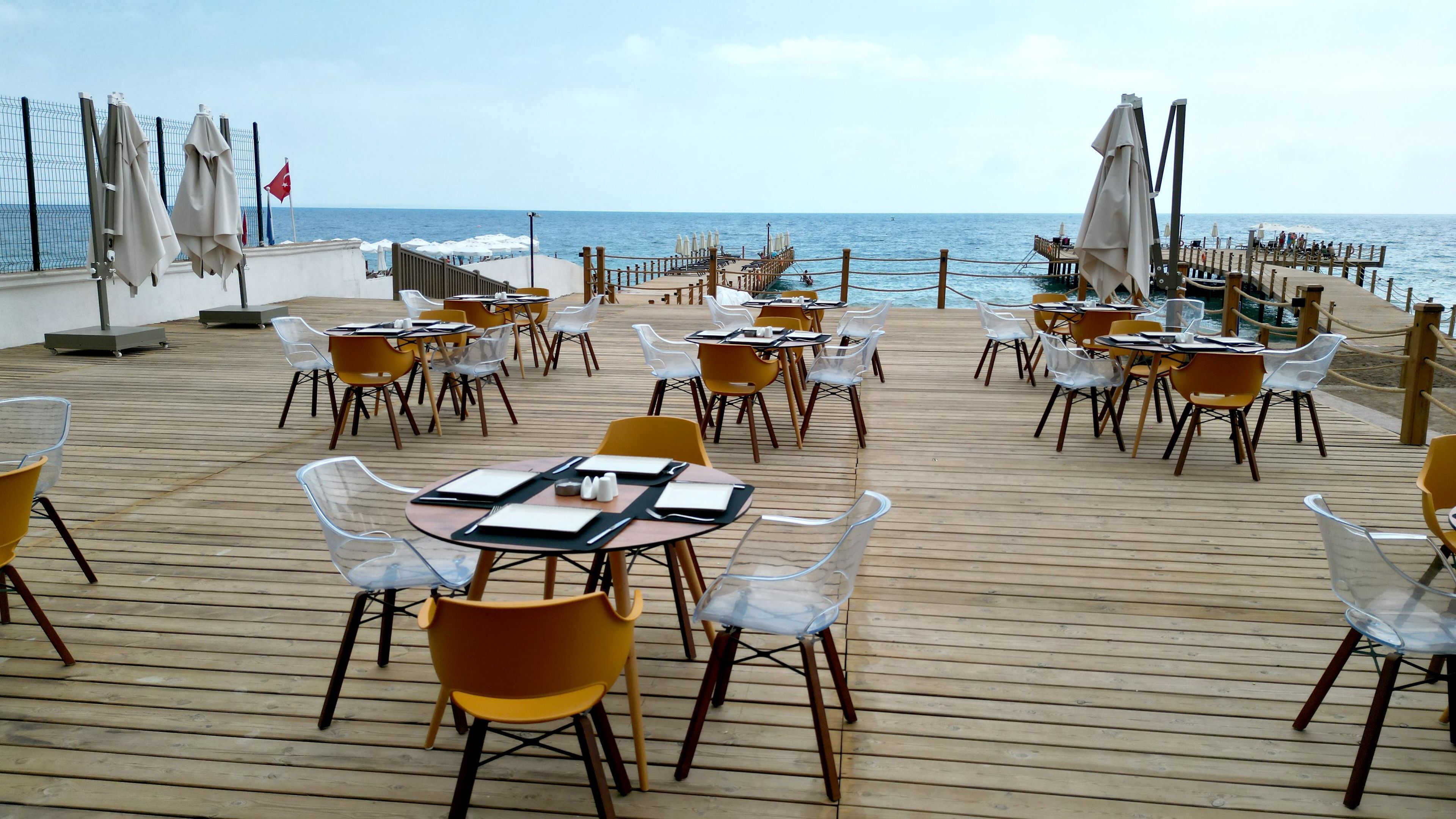 Terraza de madera con mesas y sillas, con vista al mar.