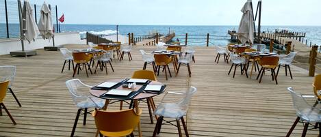 Terraza de madera con mesas y sillas, con vista al mar.