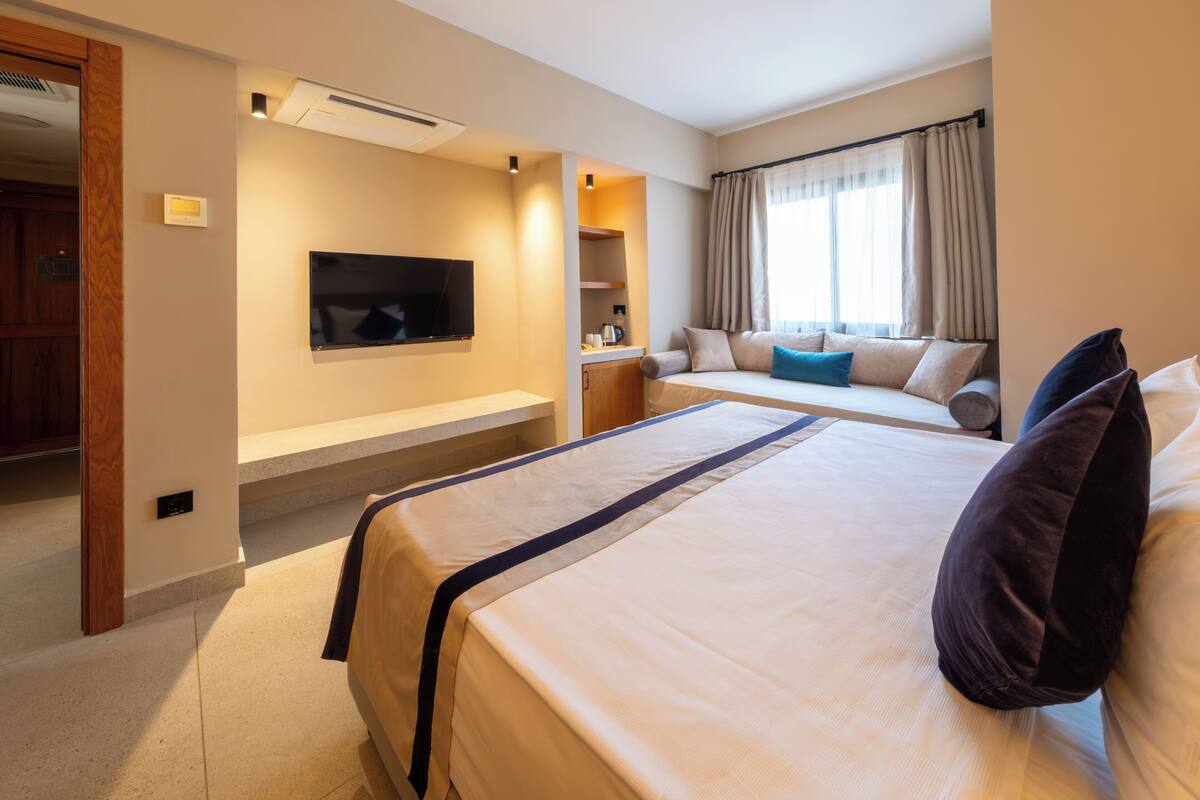 A hotel room with a large bed, a TV mounted on the wall, a seating area with a sofa, and a window with curtains.