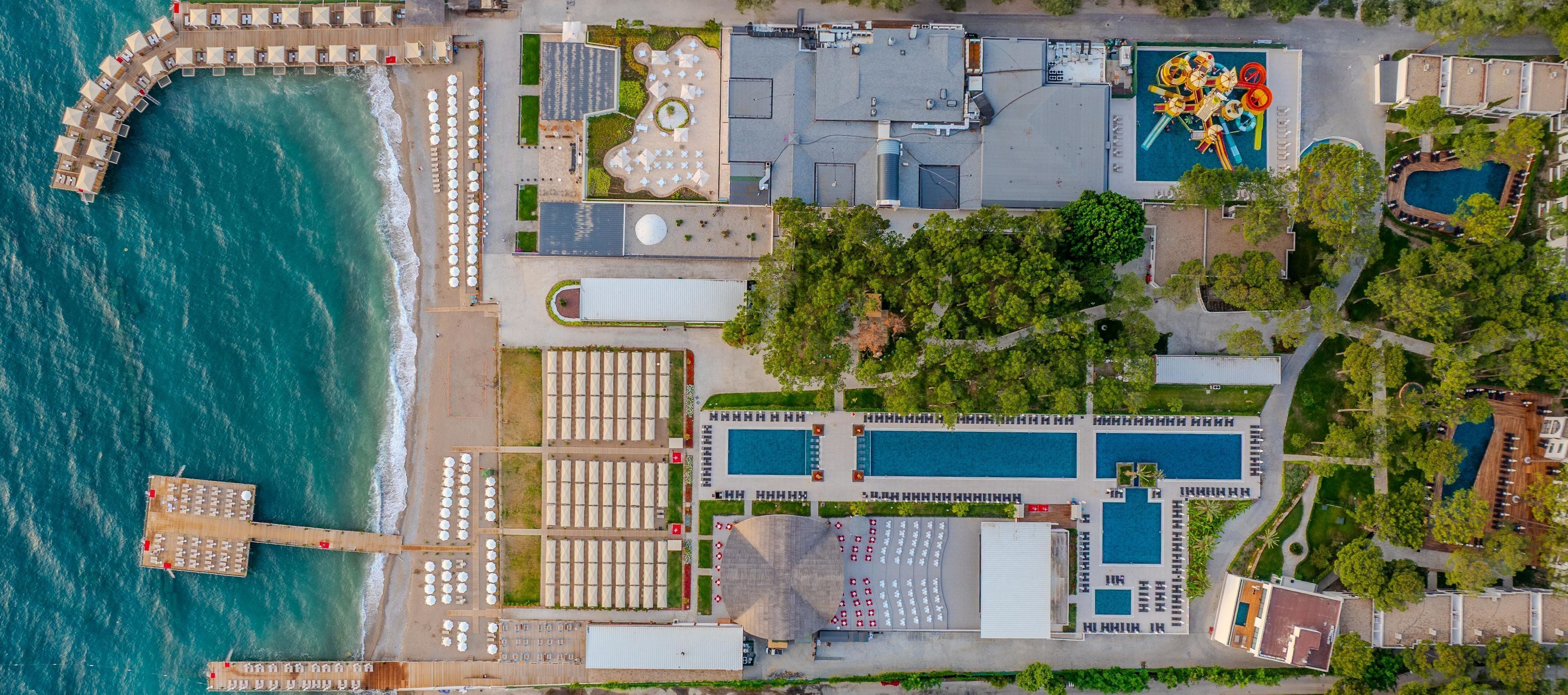 An aerial view of a resort with multiple swimming pools, a pier with sun loungers, and a large building with a rooftop pool area.