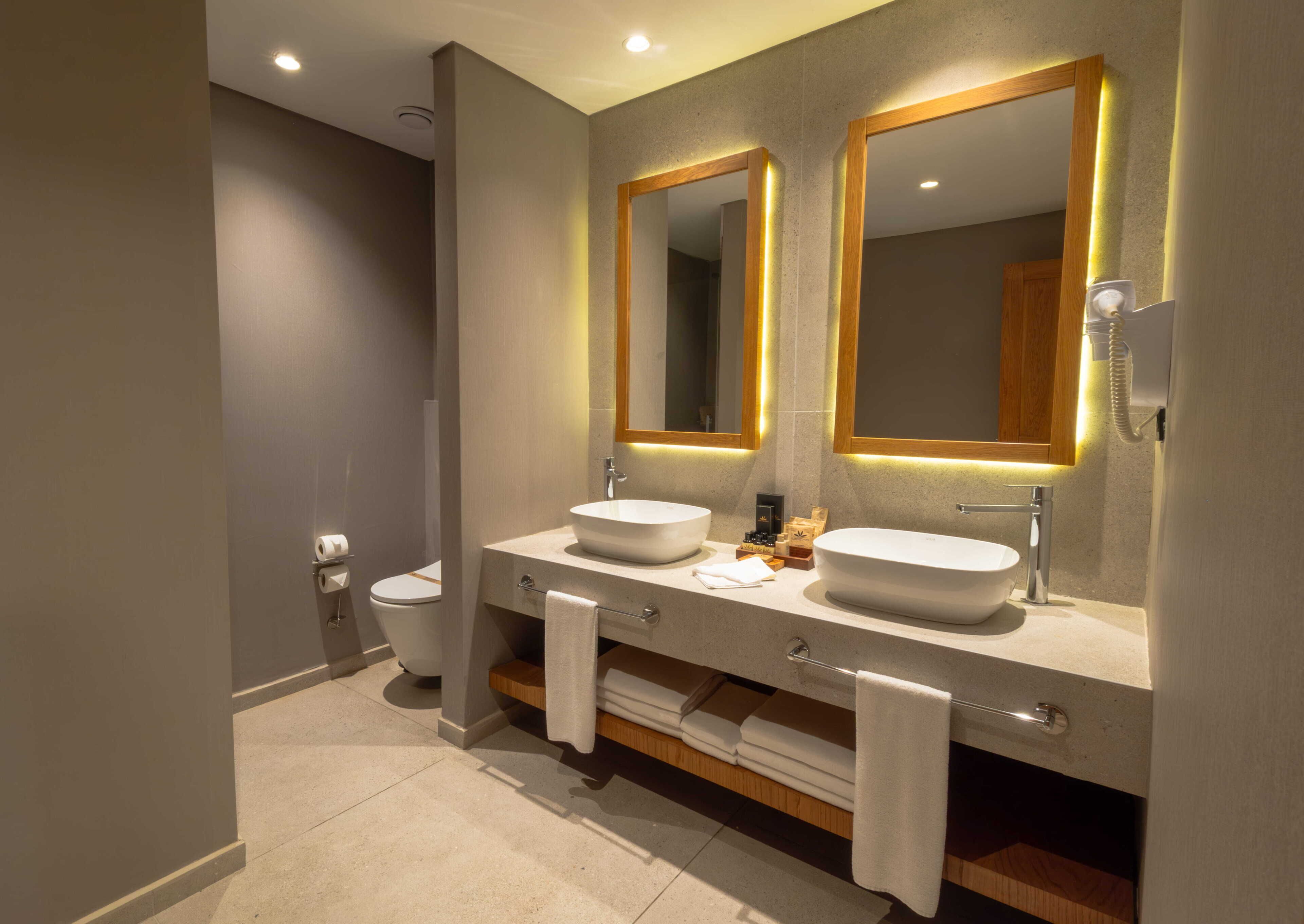 A modern bathroom with two sinks, a toilet, and a mirror with illuminated frames.