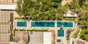 Vue aérienne d’un complexe hôtelier doté de plusieurs piscines, de chaises longues et d’un grand espace couvert.