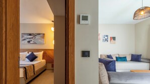 Ein modernes Hotelzimmer mit einem Bett, einer Couch und einem kleinen Tisch. Ein Gemälde hängt an der Wand, und ein Thermostat ist ebenfalls dort angebracht.