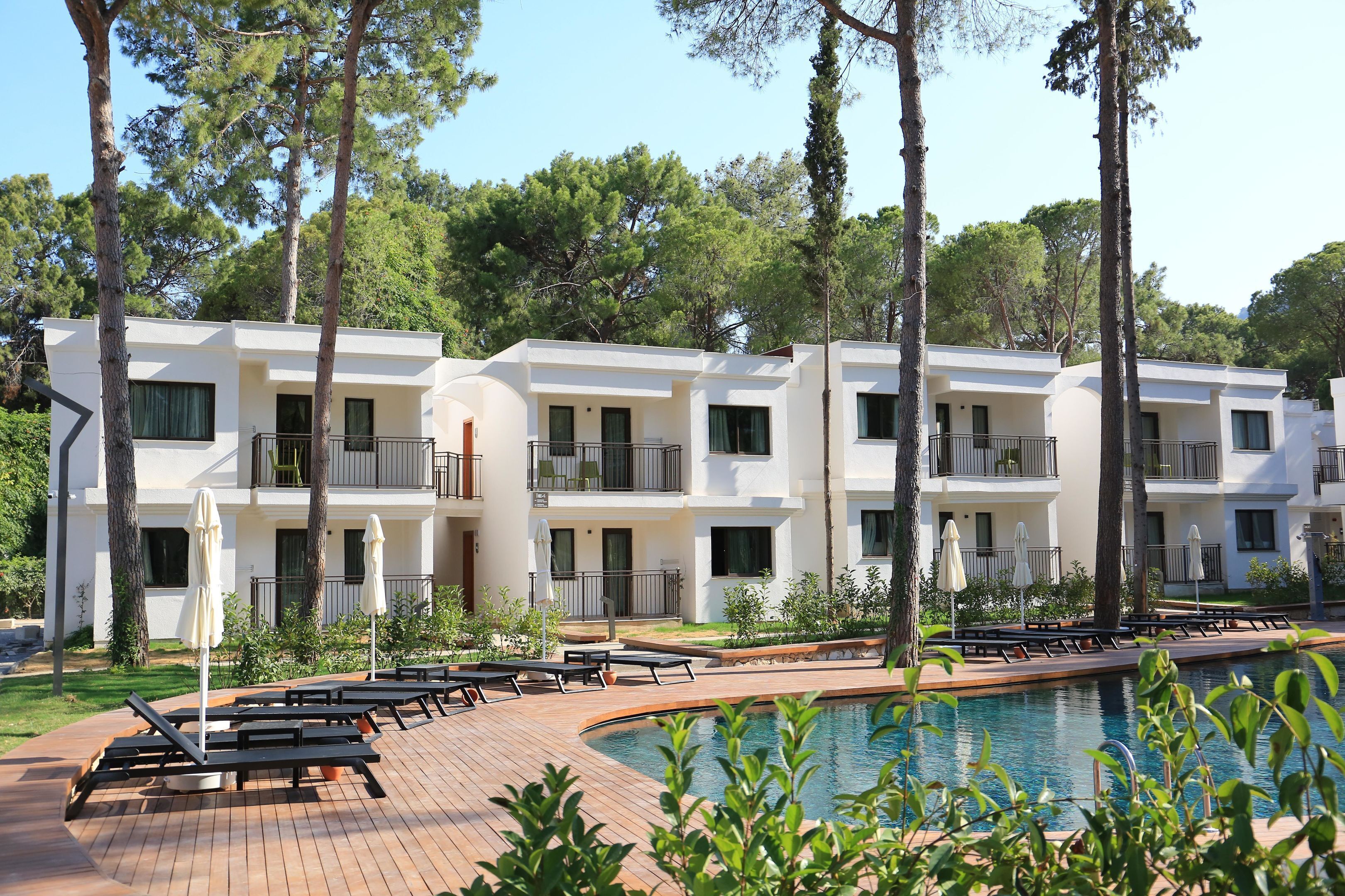 A modern hotel with multiple balconies, a swimming pool, and lounge areas.
