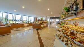 Spaziosa hall d'albergo con pavimento in marmo, ampie finestre e un'area buffet con diverse opzioni gastronomiche.