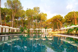 Une piscine entourée d’arbres et d’un mur de pierre, avec des chaises longues et des parasols à proximité.