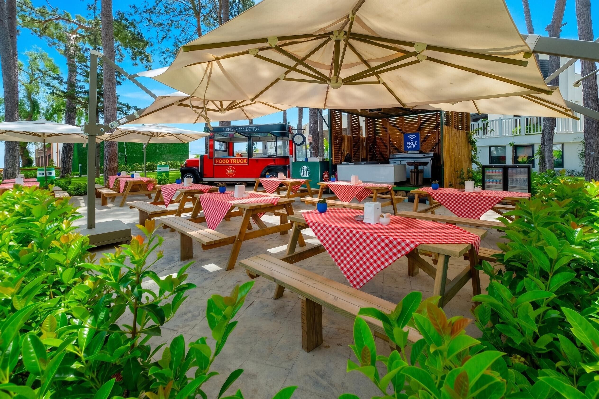 An outdoor dining area with picnic tables and umbrellas, a food truck, and a building with a sign indicating free WiFi.