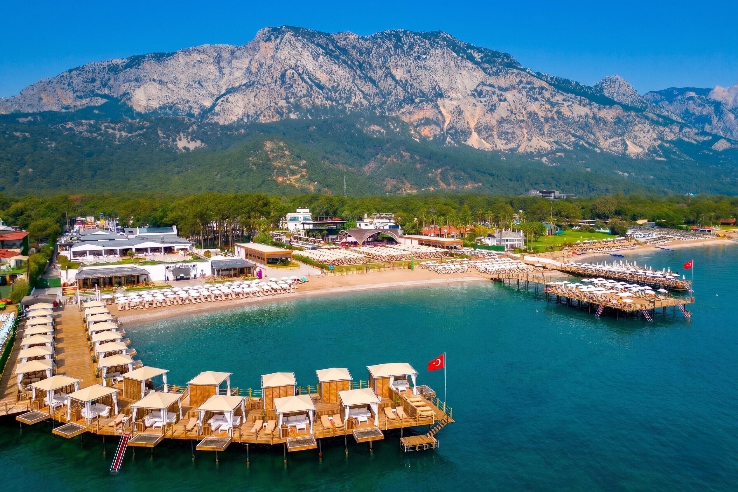 A coastal resort with wooden cabanas, a beach, and a mountain backdrop.