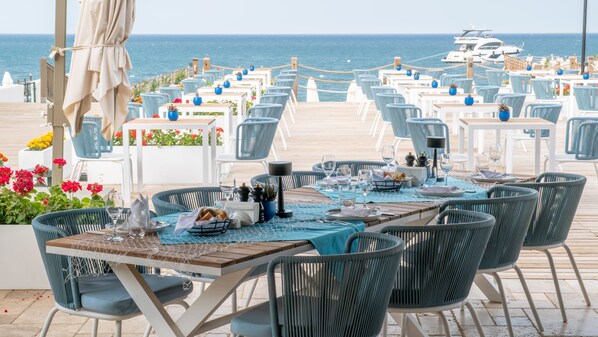 Un espace extérieur aménagé pour les repas, avec des tables et des chaises, offrant une vue sur la mer.