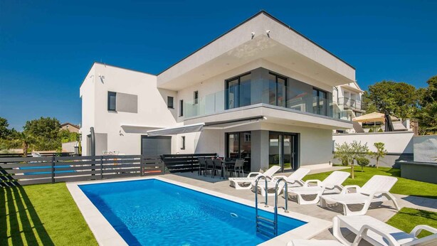 Una casa moderna de dos pisos con piscina, mobiliario exterior y un césped bien cuidado.
