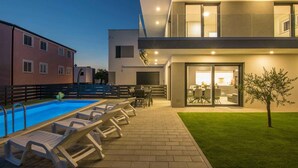 Un edificio moderno con piscina, asientos exteriores e ingreso bien iluminado.