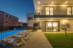 Un bâtiment moderne doté d’une piscine, d’un espace extérieur aménagé et d’une entrée bien éclairée.