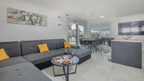 Una sala de estar moderna con un sofá seccional gris, una mesa redonda con frutas y bebidas, y un televisor de pantalla plana montado en la pared.