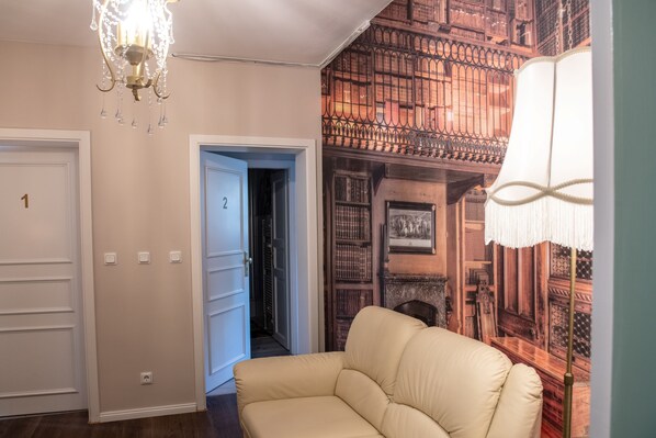 Un pasillo con un sofá color beige, un candelabro y un mural de una estantería.