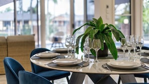 Un espace repas avec des tables rondes dressées pour un repas, agrémenté de verres et d’assiettes transparents, d’une plante en pot et offrant une vue sur l’extérieur.