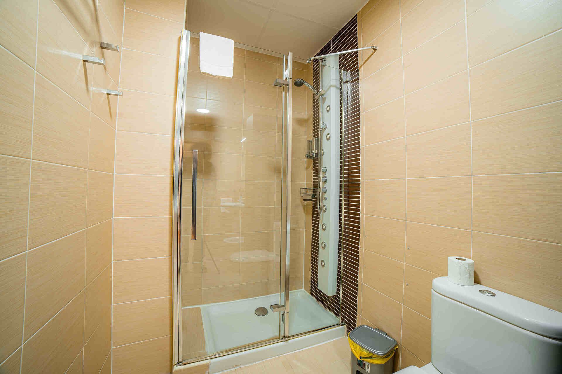 Un vestuario con ducha de vidrio, inodoro y cubo de basura en un baño con azulejos.