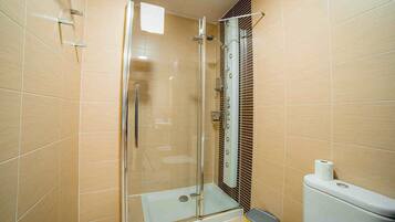 Un vestuario con ducha de vidrio, inodoro y cubo de basura en un baño con azulejos.