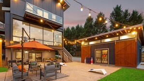 A modern outdoor patio area with a seating arrangement, a covered dining space, and a large wooden barn-like structure. - Blue Haven w/Game Room, Hot Tub & Optional Boat Rental (Mooresville)
