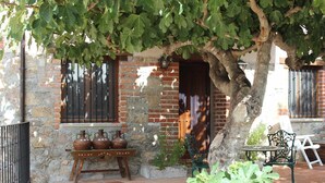 Un edificio rústico de ladrillo, una mesa de madera con cerámica y un banco bajo un árbol.