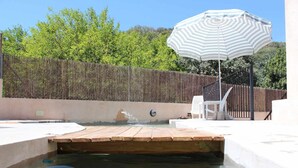 Una piscina con cubierta de madera, una fuente de agua y un paraguas a rayas.