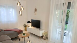 A modern living room with a sofa, a coffee table, a TV on a white cabinet, and a plant.