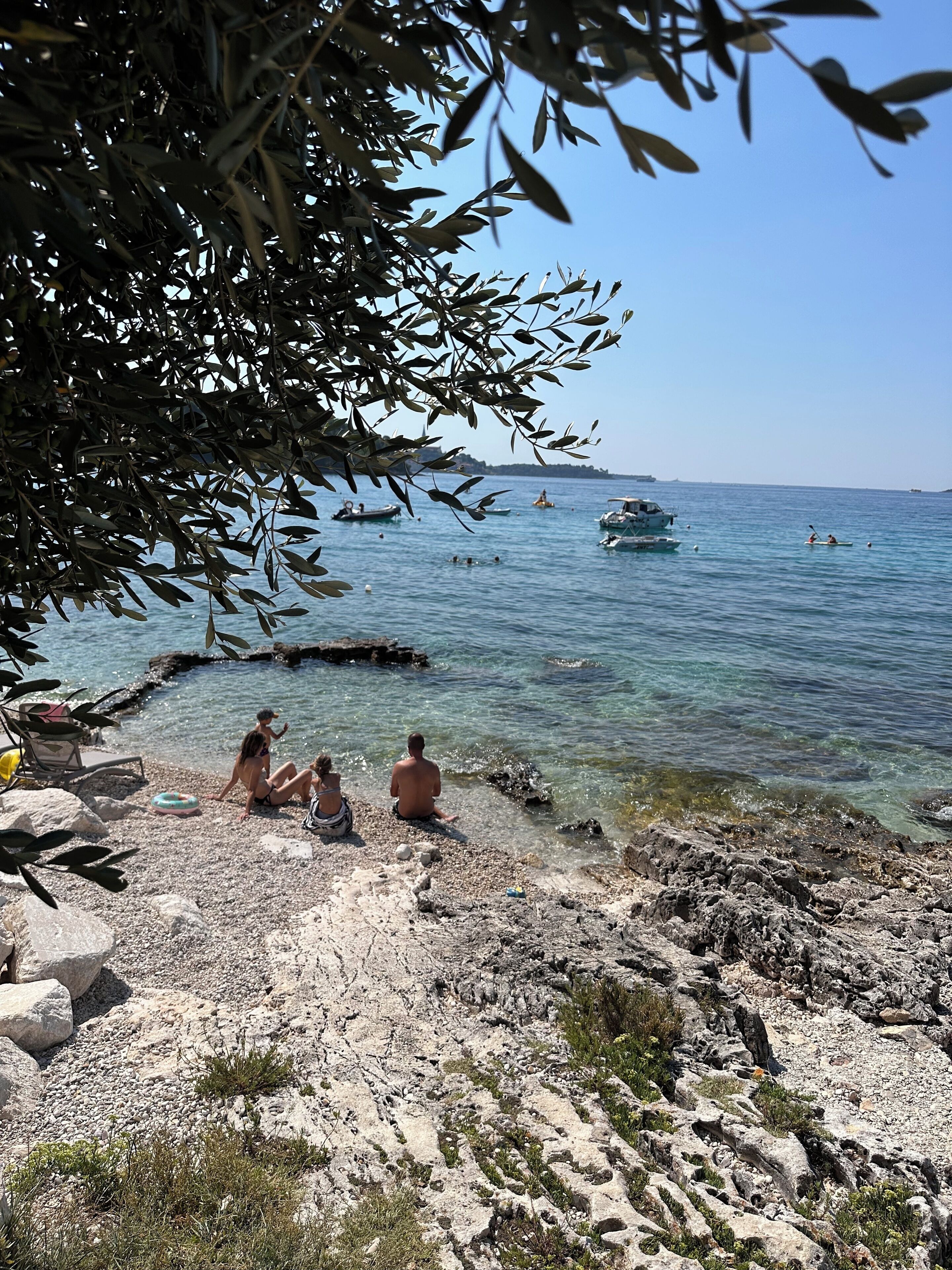 A rocky beach with clear water, boats, and people.