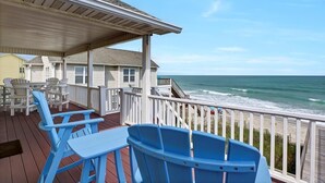 A covered deck with blue chairs and tables, overlooking the ocean. - Oceanfront Bliss - Spacious Beach Cottage for up to 11 Guests (Surf City)