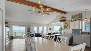 A spacious kitchen with a dining area, large windows, and a ceiling fan. - Oceanfront Bliss - Spacious Beach Cottage for up to 11 Guests (Surf City)