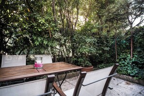 An outdoor patio with a wooden table and chairs, surrounded by dense foliage and trees.