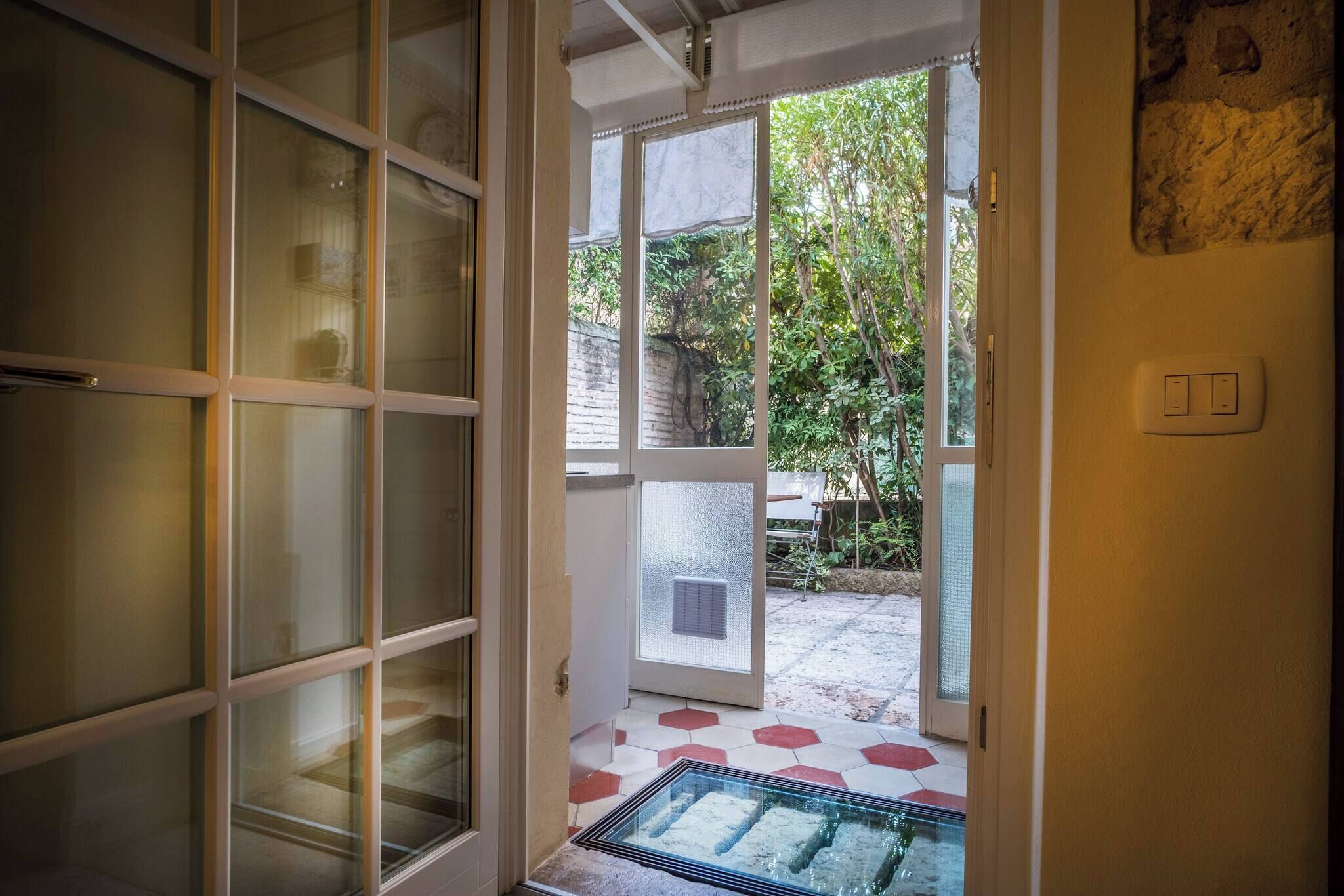 A doorway leading to a covered outdoor area with a glass door, a tiled floor, and a wall-mounted light switch.