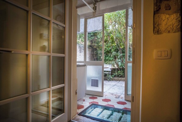 A doorway leading to a covered outdoor area with a glass door, a tiled floor, and a wall-mounted light switch.