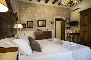 A bedroom with a stone wall, wooden furniture, a bed with pillows, a dresser, a mirror, a television, and a chandelier.