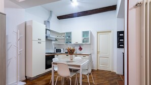 Una cocina compacta con armarios blancos, una mesa de comedor con sillas y suelo de madera.