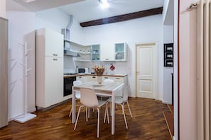 Cozinha compacta com armários brancos, uma mesa de jantar com cadeiras e piso de madeira.