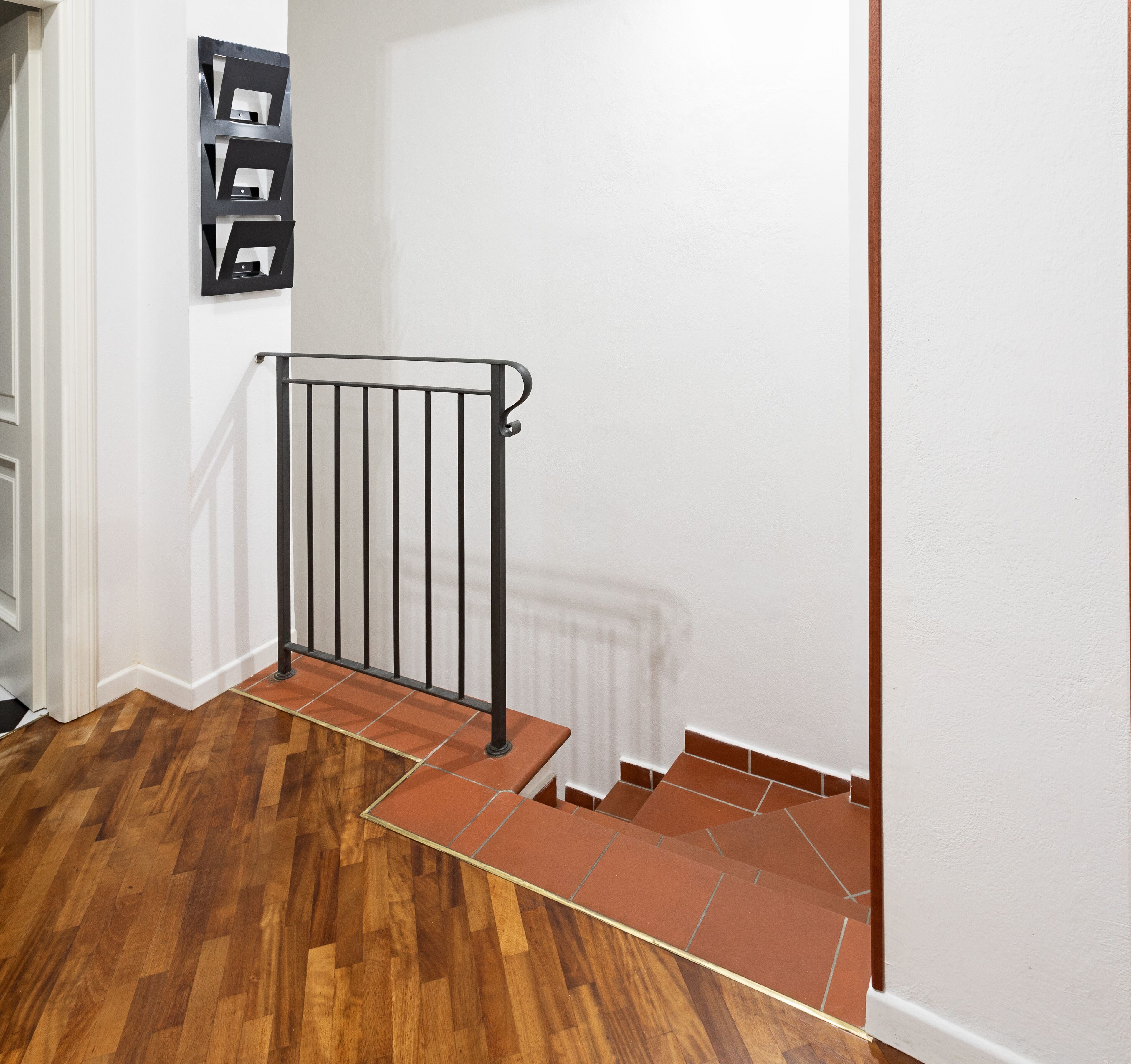 A staircase with a metal railing, wooden floor, and red-tiled steps.