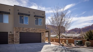 Une maison moderne à deux étages, dotée d’un garage, d’une façade en pierre et offrant une vue sur les montagnes.