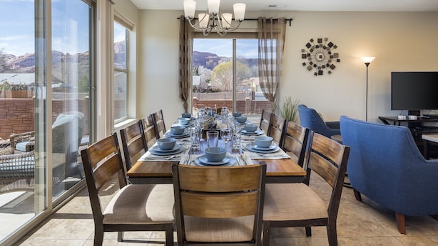 Un coin repas avec une grande table dressée pour six personnes, entourée de chaises, d’un lustre et d’un téléviseur posé sur un meuble.